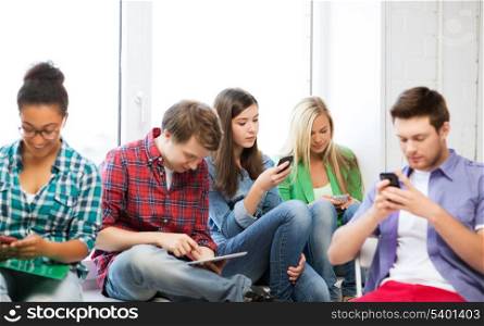 education concept - students looking into phones and tablet pc at school