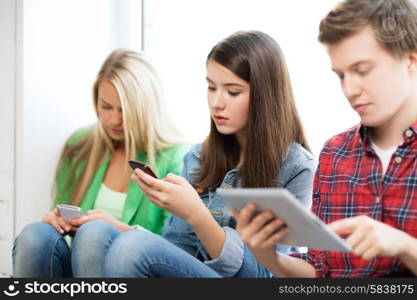 education concept - students looking into phones and tablet pc at school