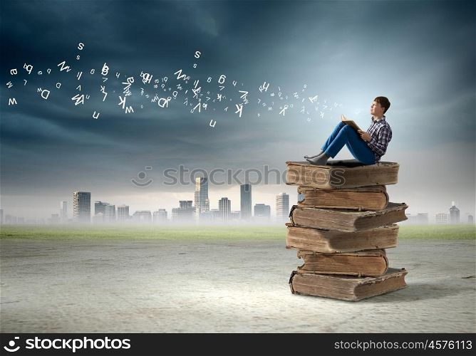 Education concept. Teenager sitting on pile of books and reading