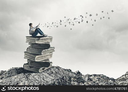 Education concept. Teenager sitting on pile of books and reading