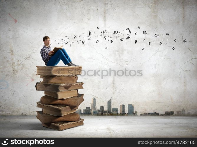 Education concept. Teenager sitting on pile of books and reading