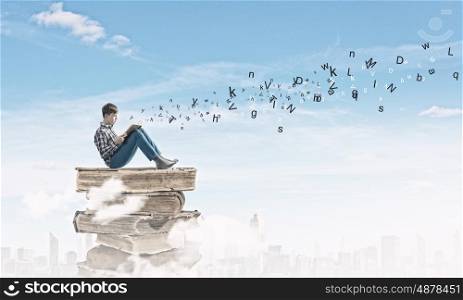 Education concept. Teenager sitting on pile of books and reading