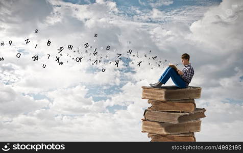 Education concept. Teenager sitting on pile of books and reading