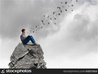 Education concept. Teenager sitting on top of rock and reading