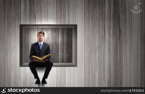 Education concept. Young businessman sitting in cube with book