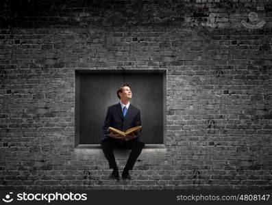 Education concept. Young businessman sitting in cube with book