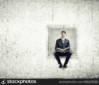 Education concept. Young businessman sitting in cube with book