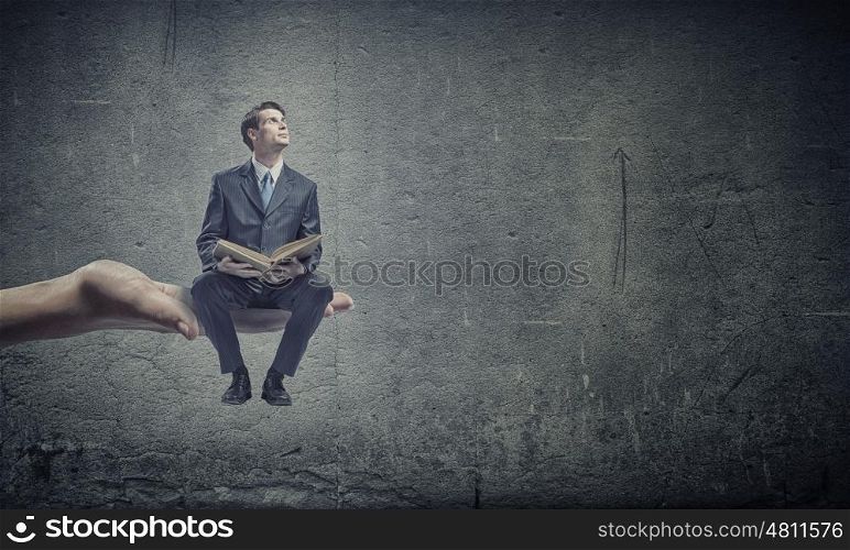 Education concept. Young businessman sitting in palm with book