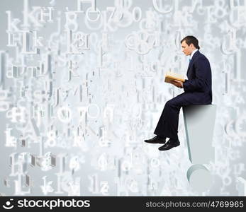 Education concept. Young businessman sitting on exclamation mark and reading book