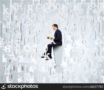 Education concept. Young businessman sitting on exclamation mark and reading book