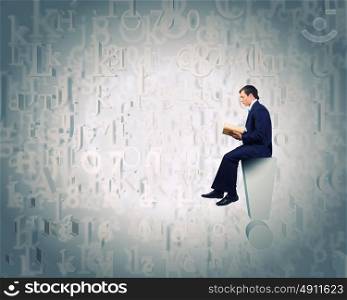 Education concept. Young businessman sitting on exclamation mark and reading book