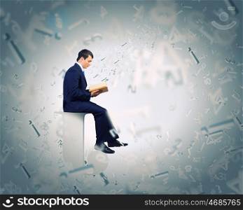 Education concept. Young businessman sitting on letter and reading book