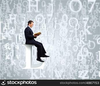 Education concept. Young businessman sitting on letter and reading book