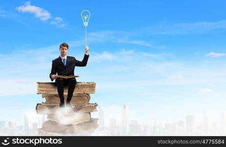 Education concept. Young businessman sitting on pile of books