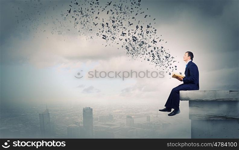 Education concept. Young businessman sitting on top of building and reading book