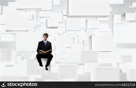Education concept. Young businessman sitting on white cube with book