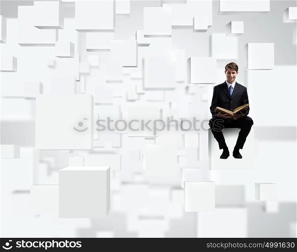 Education concept. Young businessman sitting on white cube with book