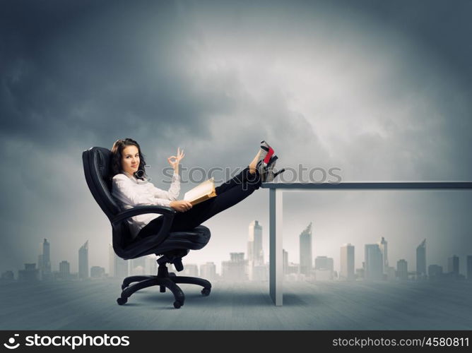 Education concept. Young businesswoman sitting in chair with legs on table and reading book