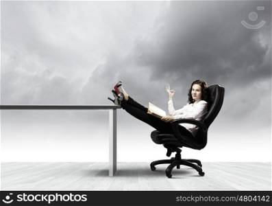 Education concept. Young businesswoman sitting in chair with legs on table and reading book