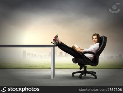 Education concept. Young businesswoman sitting in chair with legs on table and reading book