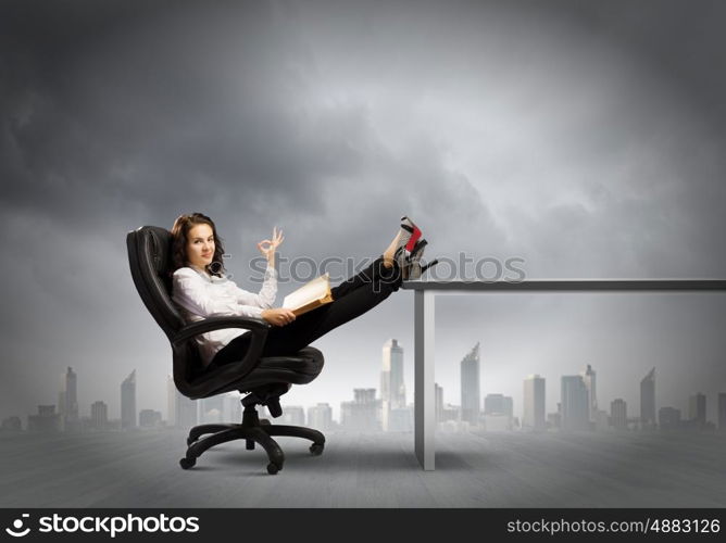 Education concept. Young businesswoman sitting in chair with legs on table and reading book