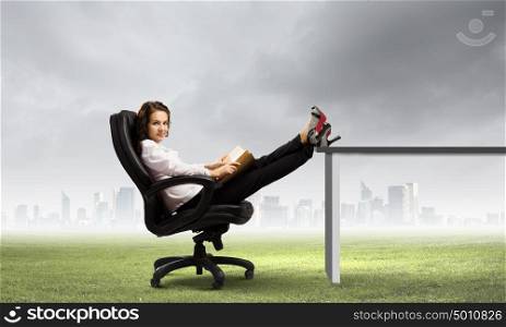 Education concept. Young businesswoman sitting in chair with legs on table and reading book