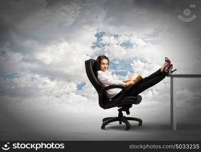 Education concept. Young businesswoman sitting in chair with legs on table and reading book