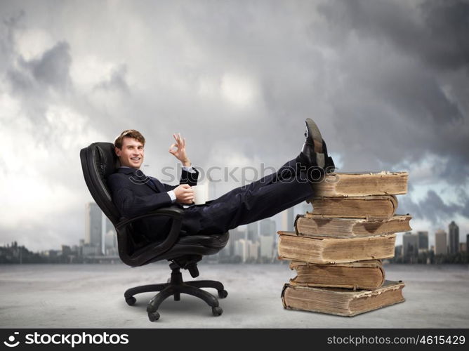 Education concept. Young handsome businessman sitting in chair with his legs on pile of books