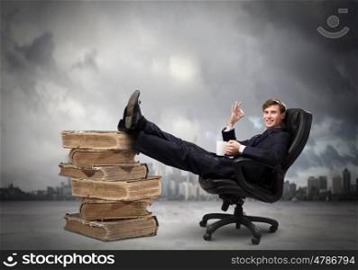 Education concept. Young handsome businessman sitting in chair with his legs on pile of books