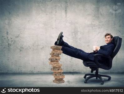 Education concept. Young handsome businessman sitting in chair with his legs on pile of books