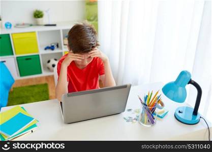 education, cyberbullying and people concept - sad student boy with on laptop computer at home suffering of bullying. tired student boy with laptop computer at home