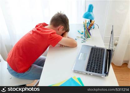 education, cyberbullying and people concept - tired or sad student boy with laptop computer lying on desk at home suffering from bullying. tired or sad student boy with laptop at home