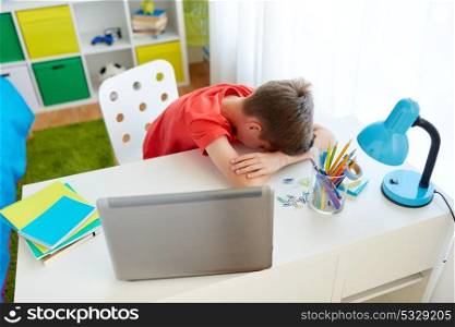 education, cyberbullying and people concept - tired or sad student boy with laptop computer lying on desk at home suffering from bullying. tired or sad student boy with laptop at home