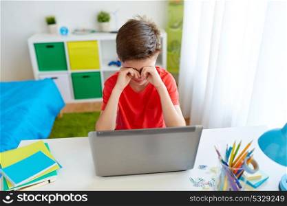 education, cyberbullying, technology and people concept - tired or crying student boy with on laptop computer at home rubbing his eyes or suffering of bullying. tired student boy with laptop computer at home