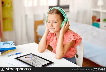 education, e-learning and school concept - happy student girl in headphones with teacher on tablet computer having online lesson at home desk. girl in headphones with tablet computer at home