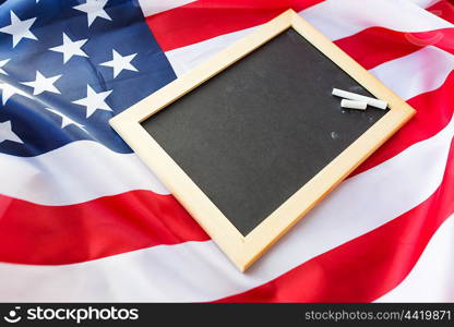 education, election, patriotism and nationalism concept - close up of blank school blackboard and chalk on american flag