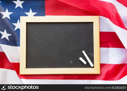 education, election, patriotism and nationalism concept - close up of blank school blackboard and chalk on american flag