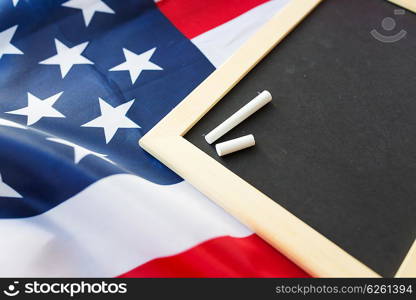 education, election, patriotism and nationalism concept - close up of blank school blackboard and chalk on american flag