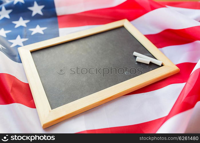 education, election, patriotism and nationalism concept - close up of blank school blackboard and chalk on american flag