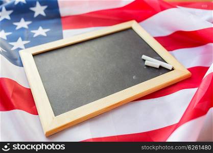 education, election, patriotism and nationalism concept - close up of blank school blackboard and chalk on american flag