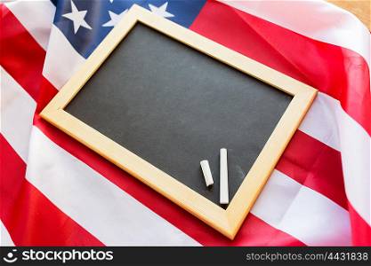 education, election, patriotism, national and memorial concept - close up of blank school blackboard and chalk on american flag