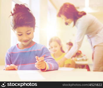 education, elementary school and children concept - happy little student girl with pen and paper writing over classrom and teacher background