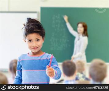education, elementary school and children concept - happy little student girl with pen over classroom and teacher writing on green blackboard background