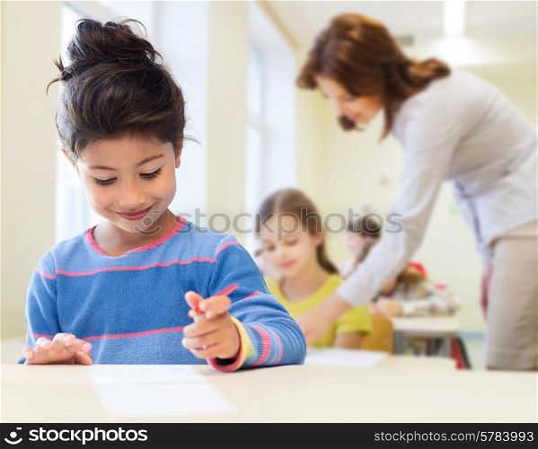 education, elementary school and children concept - happy little student girl with pen and paper writing over classrom and teacher background