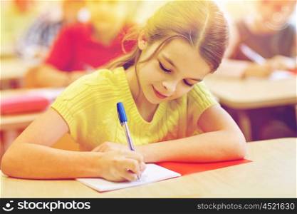 education, elementary school, learning and people concept - group of school kids with pens and notebooks writing test in classroom