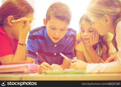 education, elementary school, learning and people concept - group of school kids with pens and papers writing in classroom