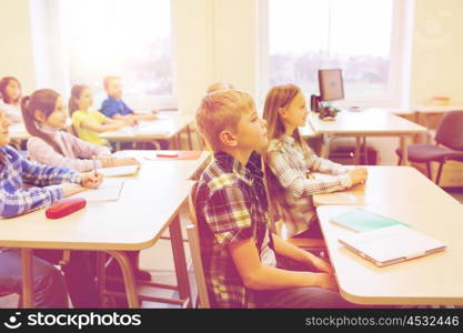 education, elementary school, learning and people concept - group of school kids with notebooks sitting in classroom