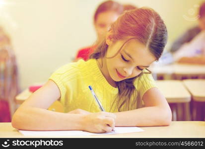 education, elementary school, learning and people concept - group of school kids with pens and notebooks writing test in classroom