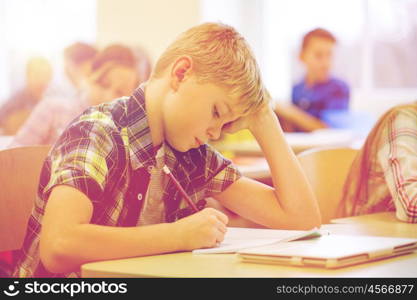 education, elementary school, learning and people concept - group of school kids with pens and notebooks writing test in classroom