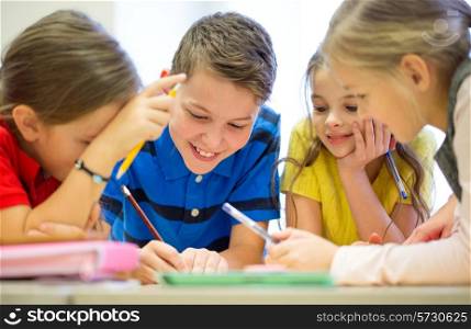 education, elementary school, learning and people concept - group of school kids with pens and papers writing in classroom